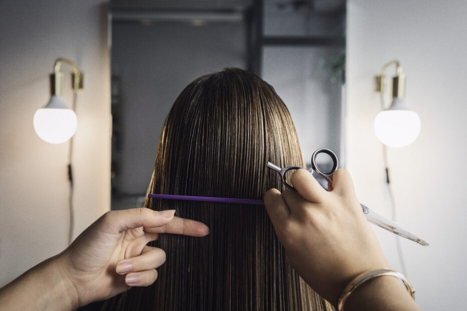 Brändikuvassa kampaaja leikkaa naisen pitkiä hiuksia.