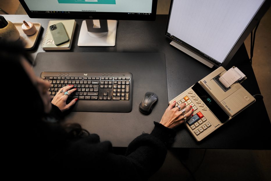 Verkkomyyntioppaan kansikuvassa yrittäjä istuu tietokoneen ääressä kädet näppäimistöllä ja laskukoneella.