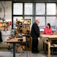 Mies ja nainen ovat puuverstaalla tietokoneen ääressä. Yrityskaupasta kertovan oppaan kuvituskuva.