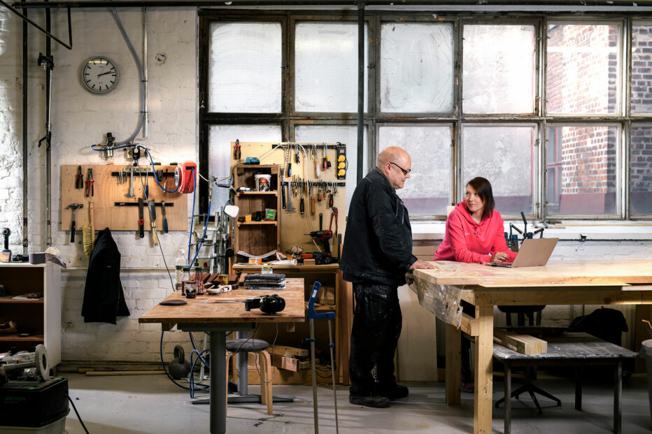 Mies ja nainen ovat puuverstaalla tietokoneen ääressä. Yrityskaupasta kertovan oppaan kuvituskuva.