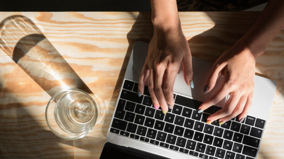 Naisen kädet kannettavan tietokoneen näppäimistöllä.